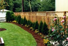 a fenced in backyard area with flowers and plants on the grass, next to a wooden bench