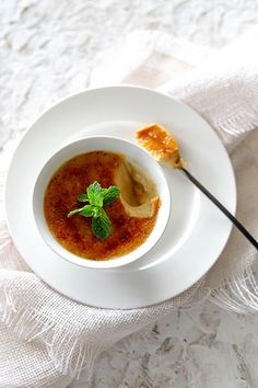 a bowl of soup with a spoon on a white table cloth next to some bread