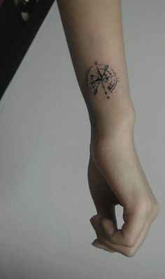 a person's arm with a small compass tattoo on the left side of their wrist