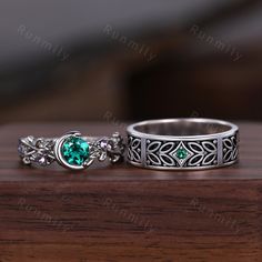 two rings with green stones on them sitting on a wooden table next to each other