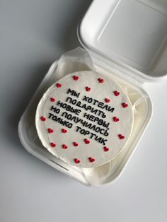 a white cake in a plastic container with writing on it and hearts around the edges