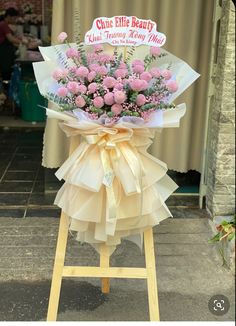 a bouquet of pink flowers sitting on top of a wooden stand in front of a store