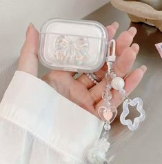 a hand holding a clear case with charms attached to it and an earring in the middle