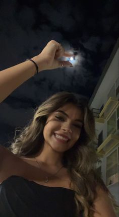 a woman in a black dress is smiling and holding her cell phone up to the camera