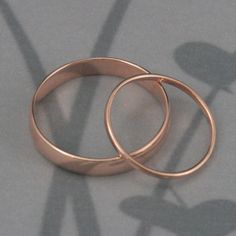 two rose gold wedding rings sitting on top of a gray surface with shadows from them