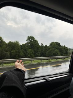 a person's hand sticking out the window of a car on a rainy day