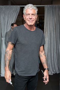 a man with grey hair and tattoos standing in front of curtains