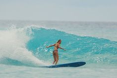 a woman riding a surfboard on top of a blue wave in the ocean with her arms out