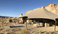 a large tent set up in the desert with chairs and tables under it, next to a swimming pool