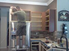 a man standing on top of a refrigerator in a kitchen next to a sink and stove