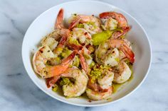 a white bowl filled with shrimp and broccoli on top of a marble counter