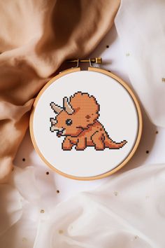 a cross - stitch pattern with an orange dinosaur on it's back, next to a tan fabric