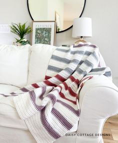 a white couch with a blanket on top of it next to a mirror and lamp