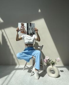 a woman sitting in a chair holding up a magazine over her face and looking at the camera