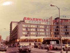 an old photo of a hotel with people walking on the sidewalk and cars driving down the street