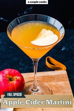 an apple cider martini is served in a coupe glass on a wooden cutting board