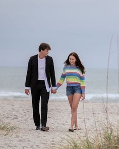 a man and woman walking on the beach holding hands