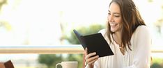 a woman sitting at a table with a tablet and coffee in front of her smiling