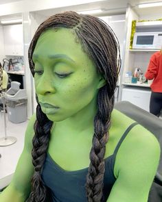 a woman with green paint on her face sitting in front of a counter and looking at the camera