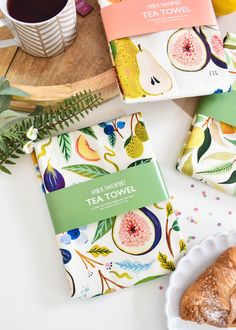 tea towels with fruit designs on them next to a cup of coffee and some pastries