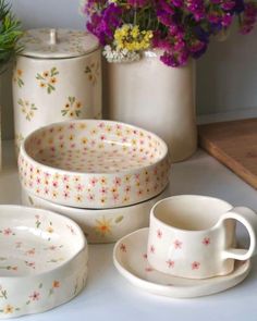 the dishes are sitting on the table with flowers in vases and containers behind them