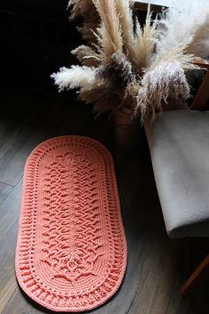 an orange crocheted rug sitting on top of a wooden floor next to a chair