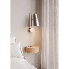 a white bed sitting next to a wall mounted light on the side of a wall