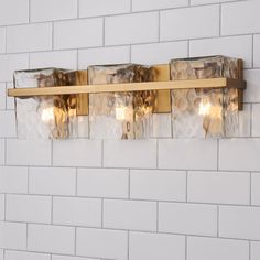 a bathroom light with three lights on the side of it and white brick wall behind it