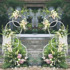 two metal archways with flowers and greenery in front of an outdoor wedding ceremony