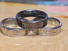 three silver rings sitting on top of a wooden table next to each other with the word texas printed on them