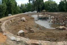 there is a picnic table and bench in the middle of this dirt field with rocks around it