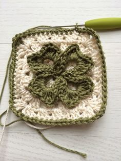 a crocheted square with a flower on it and a green handled knitting needle