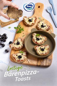 a wooden cutting board topped with mini pizzas covered in cheese and black olives