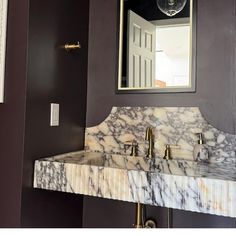 a bathroom sink with marble counter top and gold faucet, in front of a mirror