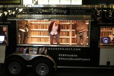 people standing in the back of a truck with books on it's display area