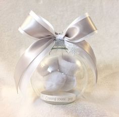 a white teddy bear in a glass ornament with a silver ribbon on top