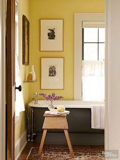 a bathroom with yellow walls and pictures above the bathtub, along with a rug on the floor