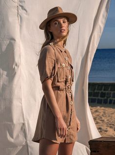 a woman wearing a hat standing in front of a white curtain and looking at the camera