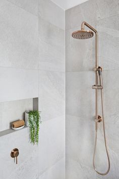 a shower head and thermostaer in a white tiled bathroom with gold faucet