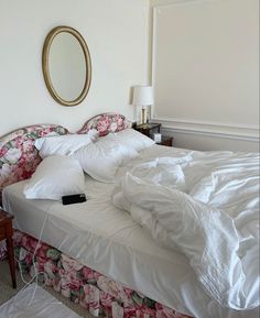 an unmade bed with white sheets and pink flowers on the bedspread next to a mirror