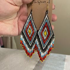 a pair of colorful beaded earrings is being held by a person's hand