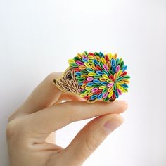 a hand holding a colorful brooch in it's right hand, with white background