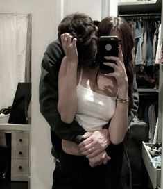 a man and woman hugging in front of a mirror taking a selfie with their cell phone