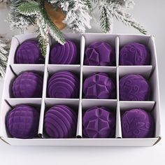 twelve purple decorated cookies in a white box on a christmas tree with pine branches behind it