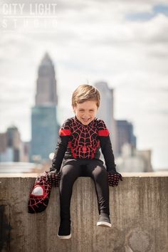 a little boy sitting on top of a cement wall wearing spiderman costume and gloves