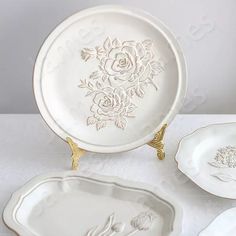 three white plates with gold designs on them and one has a flower in the center