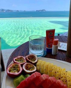 fruit and watermelon are arranged on a plate next to a glass of water