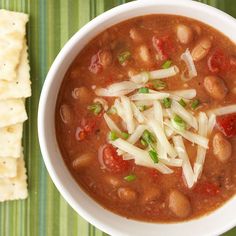 a white bowl filled with beans and cheese next to crackers on a green place mat