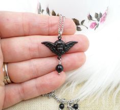 This is my handmade necklace that I created in my Wisconsin USA studio using top quality elements. The main focus is the darling cherub winged angel charm, measuring just 1 1/4 inch across.  The charm is black plated brass metal with a hollow back, accented with one top quality mystic black colored crystal pearl.  I have added a sturdy but delicate antique silver-plated satellite chain, a stainless-steel lobster clasp a 2 inch extender.  The pendant falls 1 1/4 inch below the chain and the entir Handmade Emo Style Necklace As Gift, Handmade Emo Style Necklace For Gift, Black Fairy Grunge Jewelry For Gift, Black Fairy Grunge Jewelry Gift, Fairy Grunge Black Jewelry Gift, Winged Angel, Edgy Jewelry, Black Angel, Angel Charm