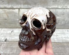 a hand holding a brown and white ceramic skull